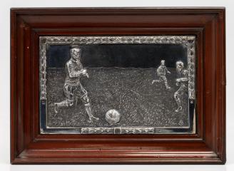 Металлическая пластина с барельефным изображением футболистов.