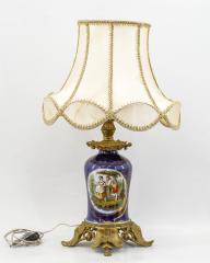 Лампа с бежевым абажуром и фарфоровым основанием с изображением в резервах пасторальной сцены и букета цветов в бронзовой оправе.